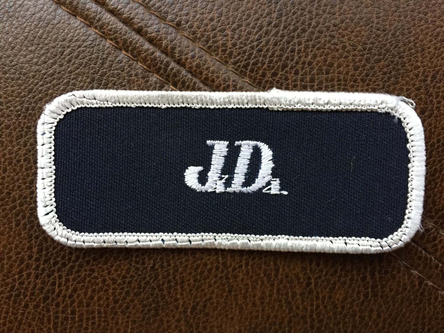 J.D. A navy blue work shirt name patch that says
