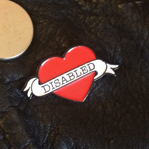 An enamel brooch in the shape of a love heart. The banner across the brooch reads