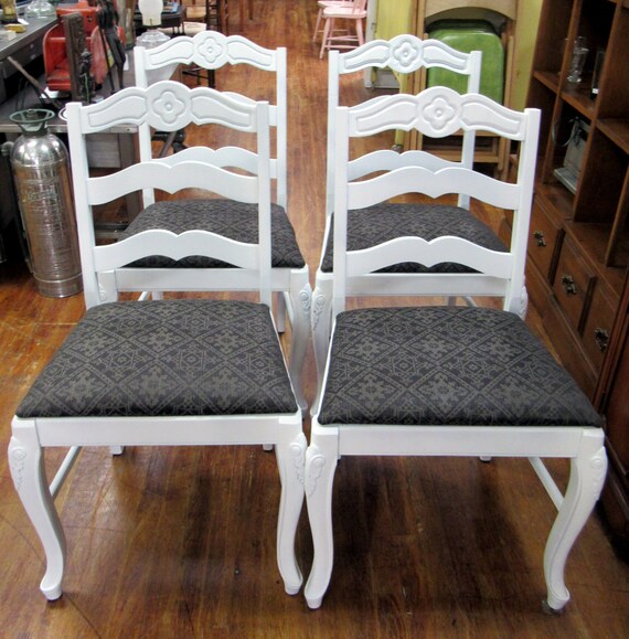 Four white chairs with black upholstery and flower carving detail
