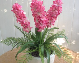White Ceramic Vase With Asymmetrical Carvings. Faux Silk Deep Rose Colored Hyacinth Plant with Green Foilage And Lacey Fern Leaves. Moss.