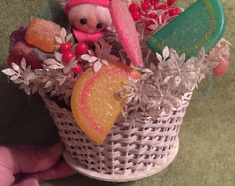 Vintage 1950s Christmas decoration. Floral arrangement with cute elf and faux candy and plants in white wicker basket. White and pastel.