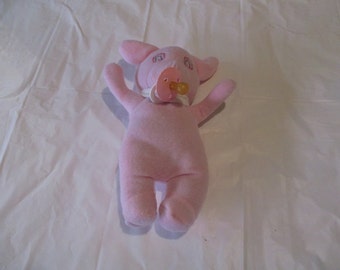 a pink pig stuffed animal holds a pacifier