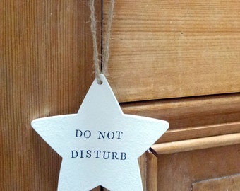 Do not disturb star shape hanging door sign in natural wood or matt white finish with hand stamped lettering and natural jute string