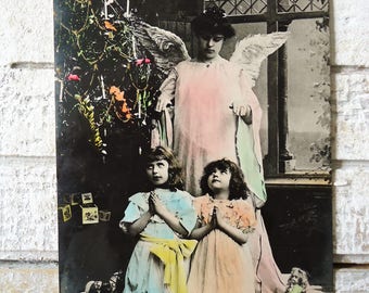 Antique Christmas postcard - Little girls child, guardian angel wings, praying Edwardian dress, tree toys doll, french hand tinted, 1900