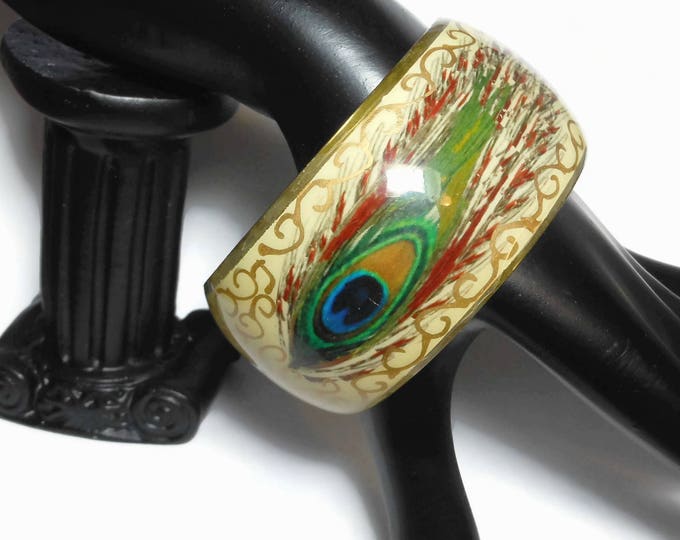 Peacock bangle bracelet, hand painted feathers on brass, wide colorful bangle, greens reds blues, cream background. gold metallic accents