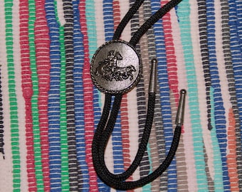 vintage bolo tie with metal emblem depicting a cowboy on horseback