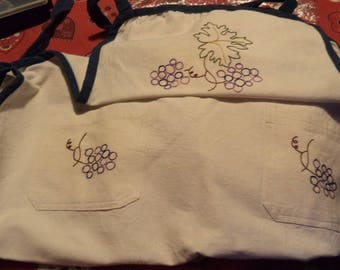 apron made of thick ecru fabric with a blue bias with embroidered grapes